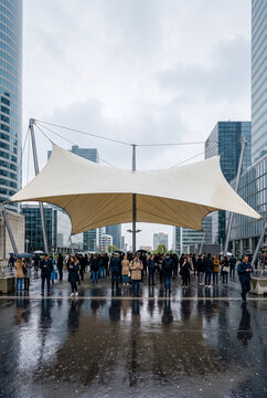 Crowd of People Sheltering from Rain Under Large White Canopy in Modern Urban Business District