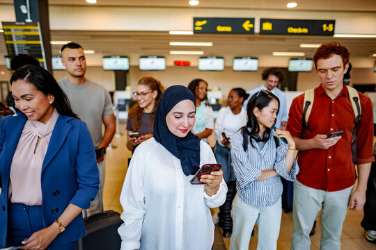 Diverse travelers waiting in airport using smartphones