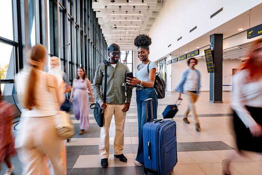 Traveling couple checking smartphone in busy airport terminal