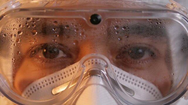 Breathing male clinician wearing PPE and N95 mask in lab, exhaling condensation fogging goggles