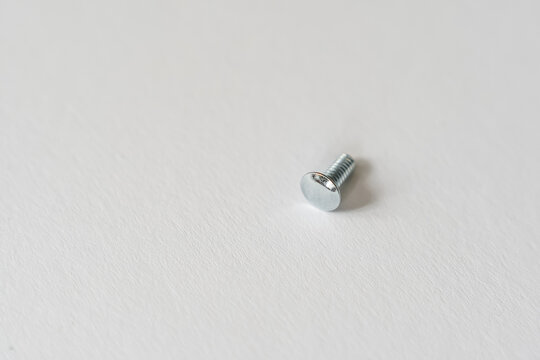Macro close up of a small silver metal bolt with a rounded head isolated on a plain background. Industrial hardware, fastening and engineering