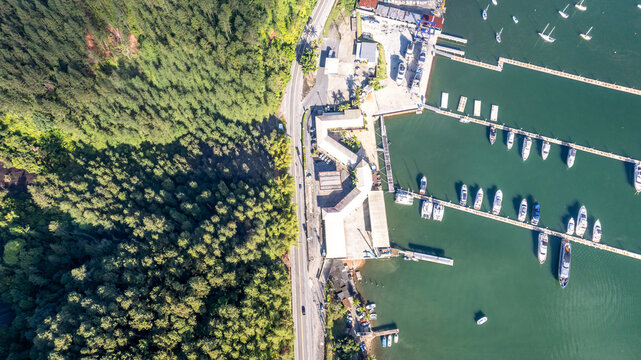 Aerial view of the marina with numerous boats docked at piers, bordered by a lush green forest and a coastal road in Angra dos Reis, Rio de Janeiro, Brazil.