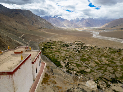 Aerial view of the historic monastery overlooking the vast Zanskar valley with its patchwork of green agricultural fields, winding river, and rugged mountains in Zanskar, Ladakh, India.