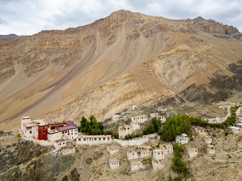 Aerial view of Karsha Monastery perched on a rocky cliffside in the Zanskar Valley, surrounded by rugged mountain slopes and scattered traditional white buildings in Zanskar, Ladakh, India.