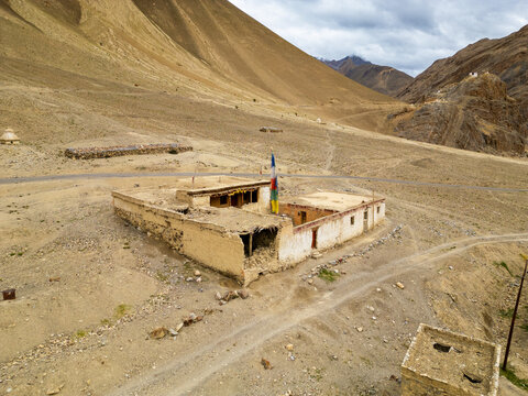 Aerial view of a traditional mud-brick building with prayer flags in a vast arid mountain landscape in Zanskar, Ladakh, India.