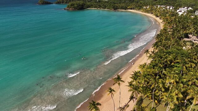 Bright aerial view of Bonita Beach with beach activity, people relaxing, turquoise sea, wave patterns and dense palms creating a tropical vacation mood.