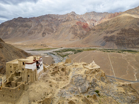 Aerial view of the ancient monastery and stupa perched on a rocky cliff overlooking the arid Zanskar valley with rugged mountains in the background, Zanskar, Ladakh, India.