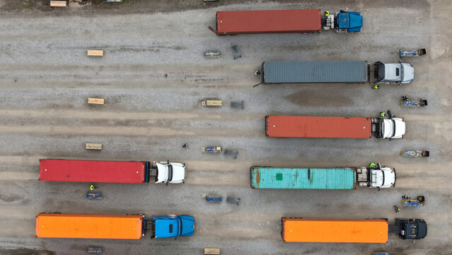 Aerial view of semi-trucks with colorful shipping containers parked in rows on a gravel logistics yard in Columbus, Ohio, United States.