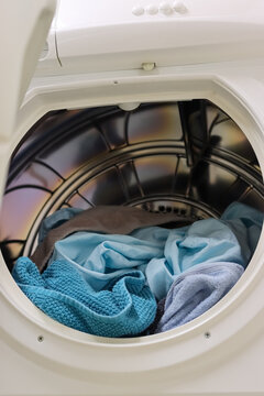Machine drying laundry at home. Clean, dry towels and bed sheets in various shades of blue inside an old but still functional tumble dryer. A tumble dryer is a great help, especially in damp weather.
