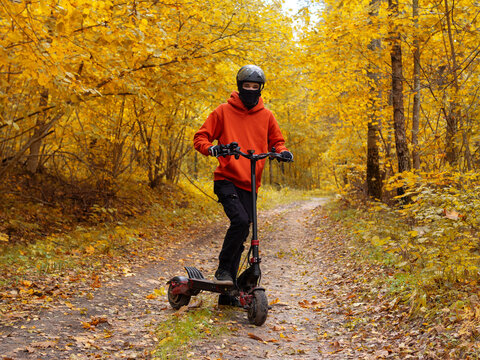 young man rides an electric scooter in an autumn forest