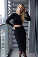 Fototapeta premium Elegant Young Woman on Modern Balcony in Black Fashion Outfit and Sheer Tights