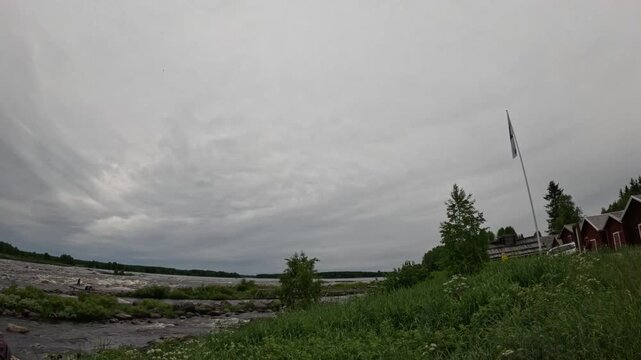 Scenic view of Kukkolankoski rapids with red wooden houses and Finnish flag