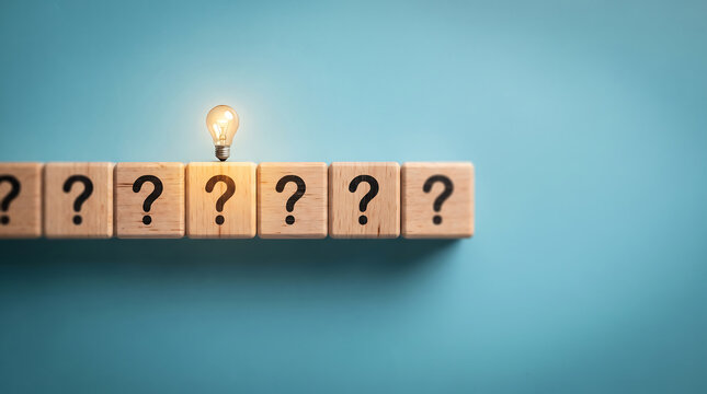 Glowing light bulb on top of a row of wooden cubes with question marks as a conceptual metaphor for innovation problem solving and finding new ideas innovation question