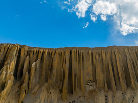 Aerial view of the dramatic, vertically eroded cliff formations in the Mustang region, featuring deep fluted ridges and sandy textures under a bright blue sky in Nepal.