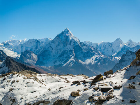 Aerial view of the snow-capped Ama Dablam mountain peak rising above the rugged Himalayan landscape under a clear blue sky in Nepal.