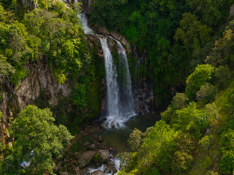 Aerial view of a cascading waterfall flowing into a pool within a lush, forested canyon in Nepal.