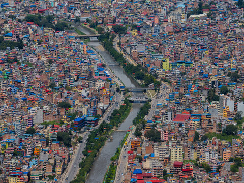 Aerial view of a dense urban cityscape featuring a river flowing through the center, multiple bridges, and closely packed multi-story buildings under a clear sky in Nepal.