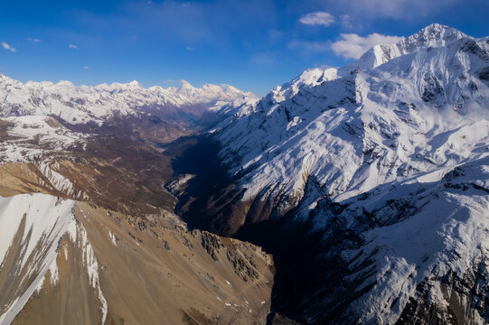 Aerial view of the snow-capped Himalayan mountain range with deep valleys, rugged peaks, and clear blue sky in Nepal.