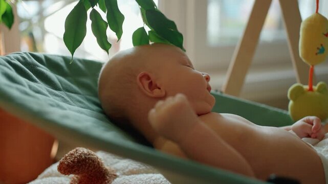 Curious newborn baby boy relaxing in a modern bouncer seat at home. The adorable infant with big blue eyes looks around, gets tired, and eventually closes his eyes to sleep