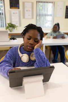 African American teenage student sitting in class using tablet stand in purple sweater with headset