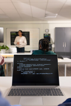 Diverse students watching Indian teacher presenting code on laptop and whiteboard in classroom
