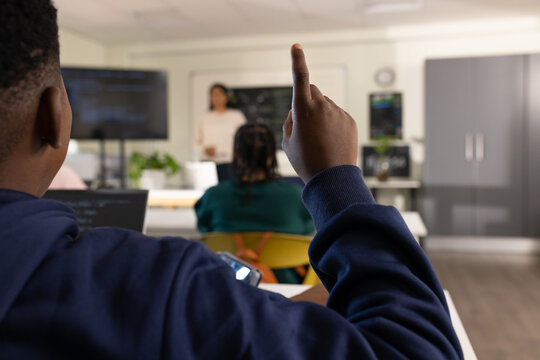 Teacher with students watching African American teen in navy hoodie raising right hand with laptop