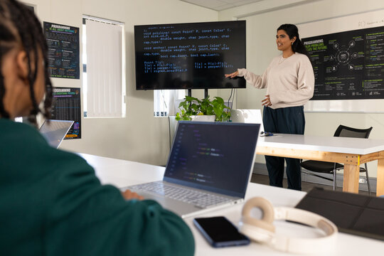 Diverse coworkers watching Indian woman presenting code on large monitor in classroom, copy space