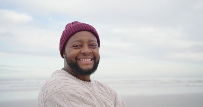 Adult man noticing camera, turning toward it on shoreline, smiling and laughing with maroon beanie