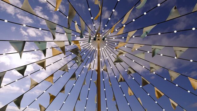 Breeze starting, pole canopy of pennant flags and lights lifting, rippling, creating festival mood