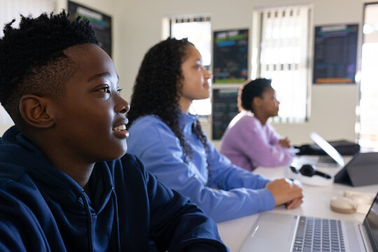 African American teens sitting at table in class, front in navy hoodie using laptops, copy space