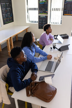 African American teenage students working on laptops and tablet at long white table in classroom
