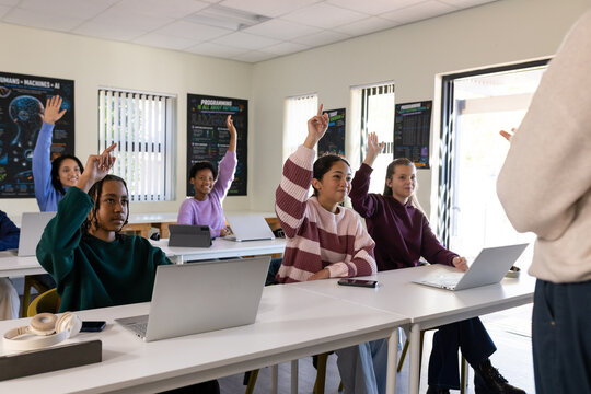 African American teens raising hands and working on laptops with phone headset AI posters at school