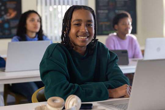 African American female students sitting at desks in classroom using laptops with beige headphones
