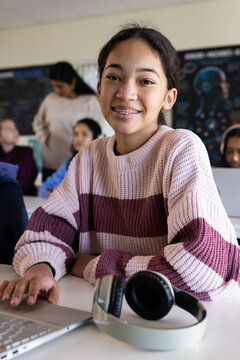 Youth African American female student smiling while typing on laptop at school desk with headphones