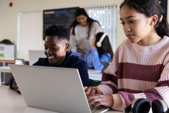 Students and teacher sitting at tables, female adolescent typing on laptop with headset, copy space