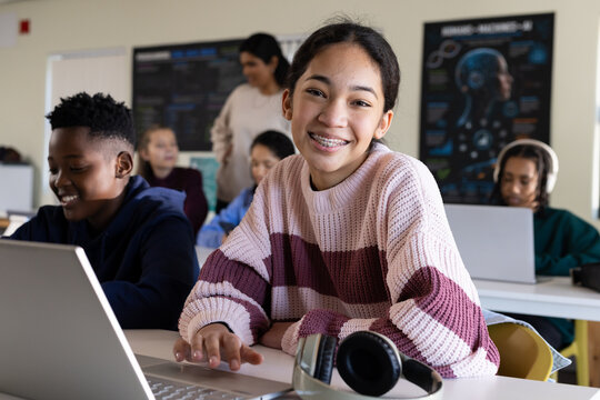 Classmates working on laptops in classroom teen female student in striped knit smiling using laptop