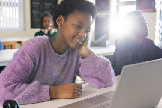 African American youth student sitting at computer lab in sweater smiling at laptop with headphones