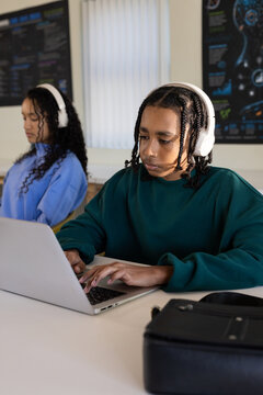 African American teenage students typing on silver laptop in classroom with white headphones