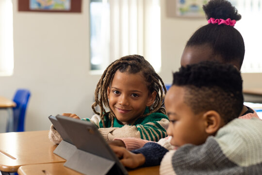 African American children sitting at wooden classroom desks using tablet folios and learning