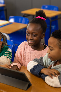 African American kids smiling and viewing tablet at school desk, girl in pink sweater and scrunchie
