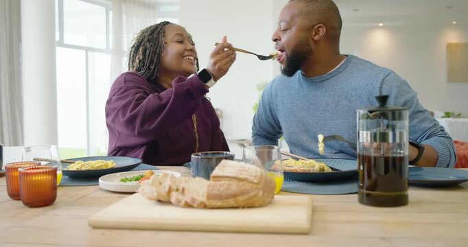 African couple at table eating bread woman looking playful lifting fork man taking bite laughing
