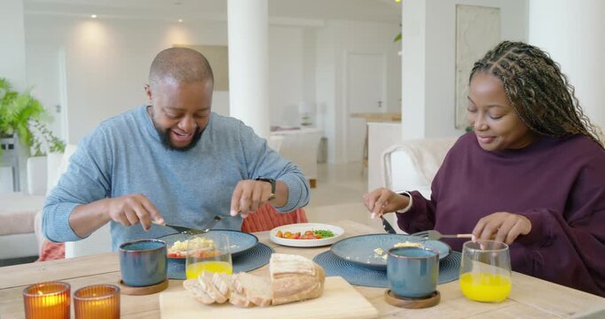 African American couple at dining table sharing meal, man gesturing, woman laughing, cutting plates