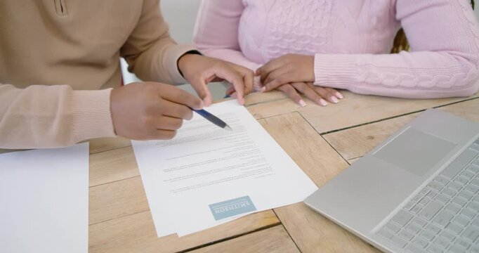 African American couple reviewing form at home pointing pen tracing lines sliding page to laptop