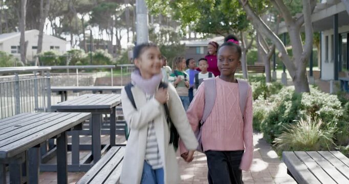 African American girls holding hands walking campus walkway leaving school with backpacks