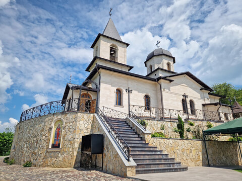Outdoor view of Varzaresti Monastery with a cobblestone courtyard and a prominent bell tower with a dark dome topped with Christian crosses under a beautiful sky