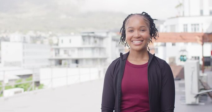 Adult African woman in jacket seeing camera on rooftop smiling laughing crossing arms showing watch