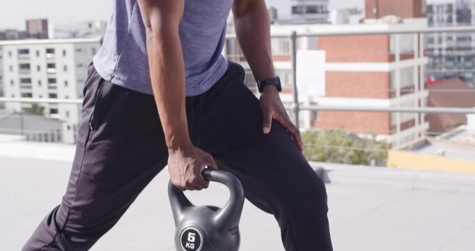 Mid-adult man rising from kneeling lunge on rooftop holding 5 KG kettlebell for strength