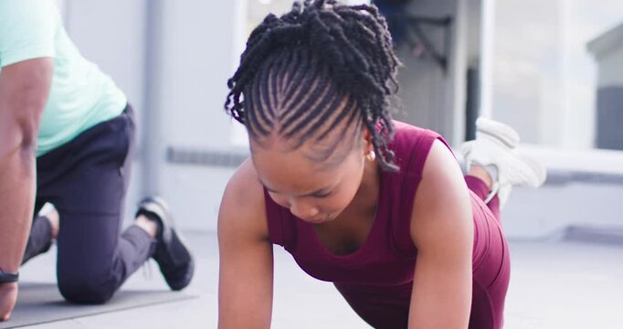 African exercise partners, woman holding modified plank in fitness studio on mat in maroon top
