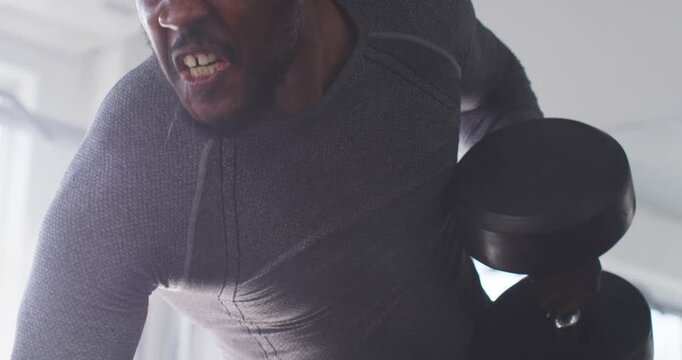 Focusing, mid-adult African man pulling dumbbell, wearing compression top for strength in gym