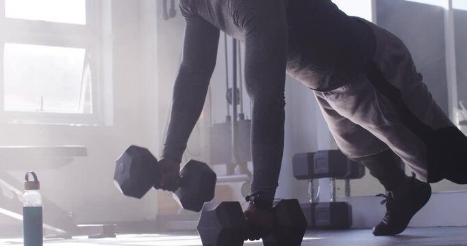African American male gripping hex dumbbells on gym floor pushing rowing building strength
